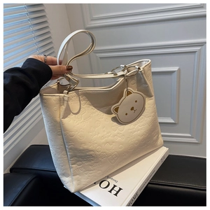 Detail of embossed patterns and bear charm on beige large capacity faux leather tote