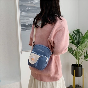 Detail of blue canvas crossbody bag with cute bear patch worn by model in pink sweater
