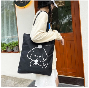 Detail of black canvas tote bag featuring white puppy print and yammy text on shoulder