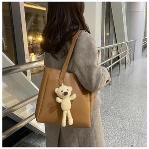 Close-up of brown leather tote bag with a cute white plush bear pendant on wide strap