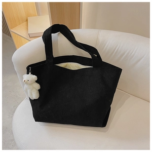 Detail of black corduroy tote bag with cute white plush bear pendant on a white sofa
