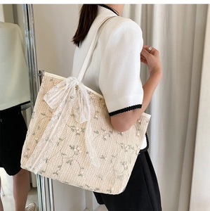 Detail of floral embroidery and white lace bow on beige woven summer tote bag