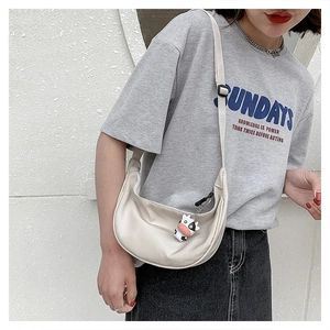 Detail of a beige nylon crescent crossbody bag with cute cow plush charm and wide strap