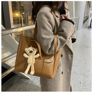 Brown soft leather tote bag detail with cute white teddy bear charm and long strap