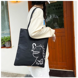Outdoor shot of a black canvas tote bag with a cute white dinosaur cartoon print