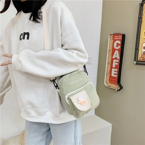 Detail of light green canvas crossbody bag featuring a cute cartoon bear patch detail