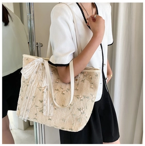 Close-up of summer straw tote bag with floral embroidery and white lace bow detail