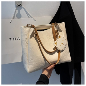 Detail of white embossed tote bag featuring cartoon patterns and brown handles with bear charm