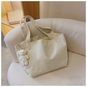 Close-up of cream corduroy tote bag with plush bear charm on a soft cream sofa