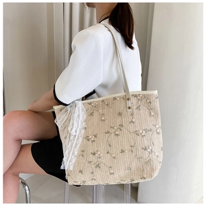 Close-up of lace bow and floral embroidery details on a straw woven tote bag