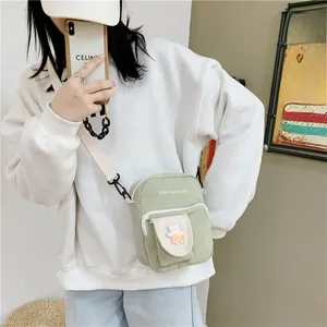 Detail of light green canvas crossbody bag with cute bear patch and adjustable strap
