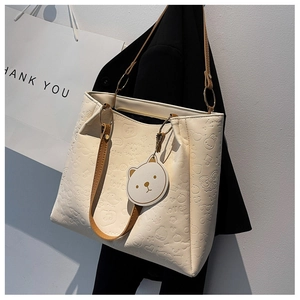 Detail of embossed tote bag featuring cartoon patterns and brown bear charm accessory