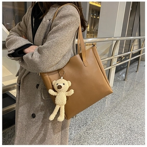 Close-up of caramel leather tote bag with a white fluffy bear keychain on the strap
