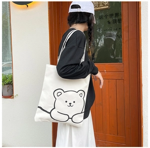 Close-up of white canvas tote bag with a minimalist cute bear graphic and shoulder straps