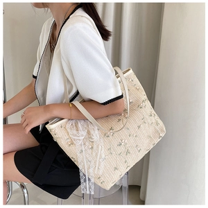 Detail of hand-woven straw tote bag with green floral embroidery and white lace trim