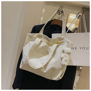 Detail of cream corduroy tote bag showing striped texture and plush bear charm