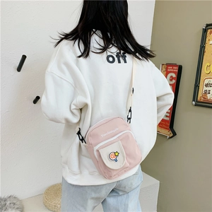 Detail of pink canvas crossbody bag with lollipop patch and adjustable shoulder strap