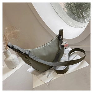 Detail view of bean green nylon crescent bag with adjustable strap and cow plush pendant