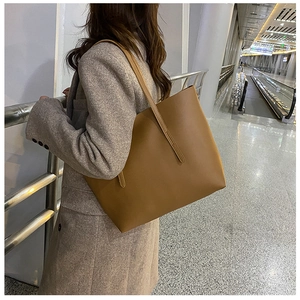 Brown faux leather tote bag with long straps worn on shoulder in modern transit setting