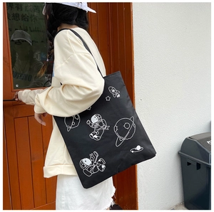 Close-up of black canvas tote bag featuring white space astronaut and planet patterns
