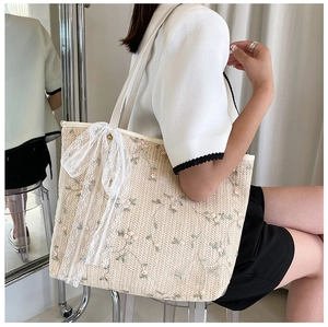 Detail of beige straw tote bag with floral embroidery and lace bow decoration