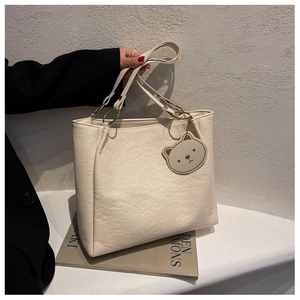 Detail of embossed cream tote bag with cartoon patterns and gold ring handle