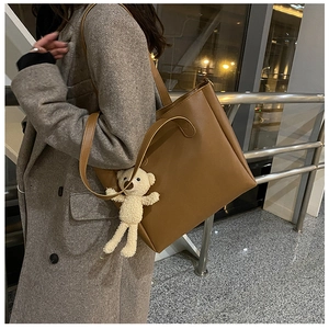 Brown soft leather tote bag with cute plush bear pendant shown on model shoulder
