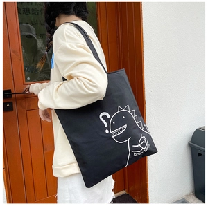 Close-up of black canvas tote bag featuring a cute white cartoon dinosaur and text design