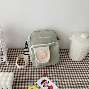 Detail of cute green canvas crossbody bag featuring a cartoon bear patch and adjustable strap