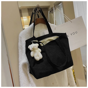 Detail of black corduroy tote bag with plush bear charm hanging in a cozy setting