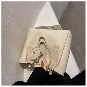 Close-up of cream leather tote bag featuring embossed cartoon motifs and bear charm