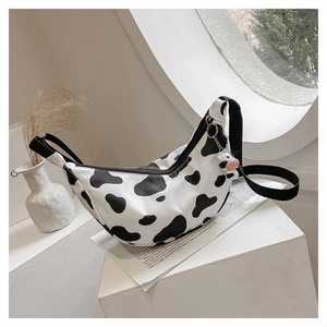Detail of cow print nylon crossbody bag featuring a plush charm and black woven strap