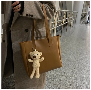 Caramel leather tote bag with a cute teddy bear charm shown in a daily lifestyle setting