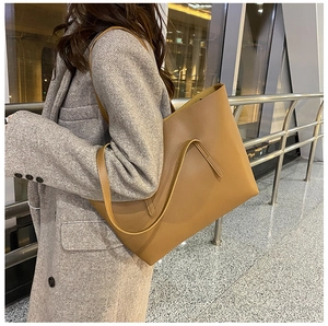 Brown leather tote bag styled with a grey coat in a modern terminal setting