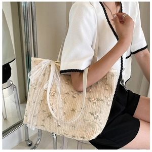Close-up of summer straw tote bag featuring floral embroidery and lace bow detail