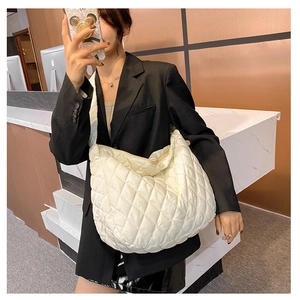 Detail view of a large cream quilted puffer shoulder bag carried by a model