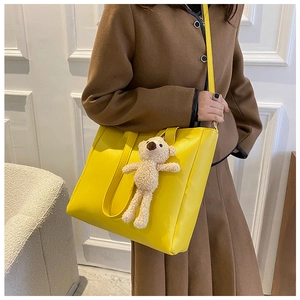 Detail of yellow soft leather tote bag featuring a cute teddy bear charm and long strap