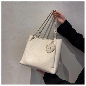 Close-up of cream embossed tote bag with cartoon patterns and gold bear pendant