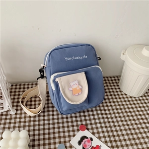 Close-up of blue canvas crossbody bag with cute bear patch on a checkered cloth
