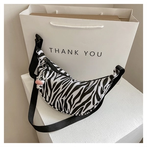 Detail of zebra print crescent crossbody bag with a cute cow charm and wide strap