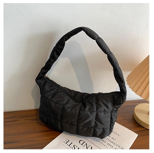 Detailed view of black quilted puffer shoulder bag on a wooden table with soft lighting