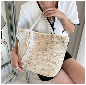 Detail of a beige woven straw tote bag featuring delicate floral embroidery and lace bow