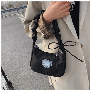 Detail of black pleated shoulder bag featuring a blue heart whale patch and lace trim