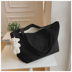 Detail of black corduroy tote bag texture with white plush bear charm and zip closure