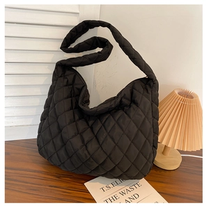 Detail of black quilted puffer tote bag with classic rhombus stitching on wooden desk