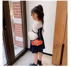 Fille portant un sac à bandoulière orange vif en forme de bonbon à pois colorés