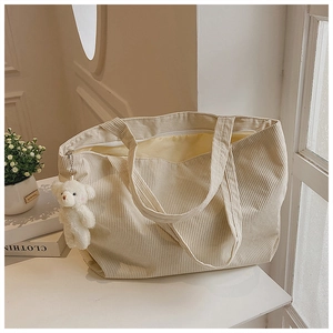 Detail of beige corduroy tote bag showing soft ribbed texture and plush bear pendant