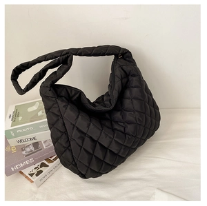 Macro view of black quilted puffer tote bag with diamond stitching on white surface