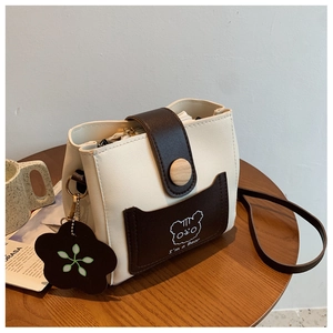 Close-up of contrast color bucket bag with cartoon bear and flower charm on a wooden table