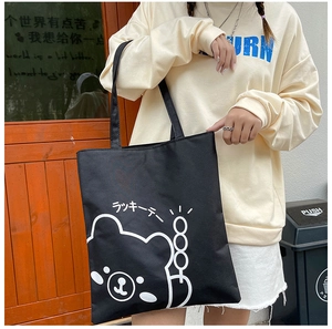 Detail view of a black canvas tote bag featuring a minimalist white cartoon bear print